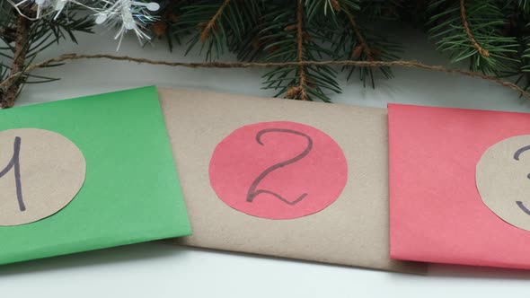 Homemade Christmas Advent Calendar Multicolored Envelopes with Numbers Lie on the Table Near Green