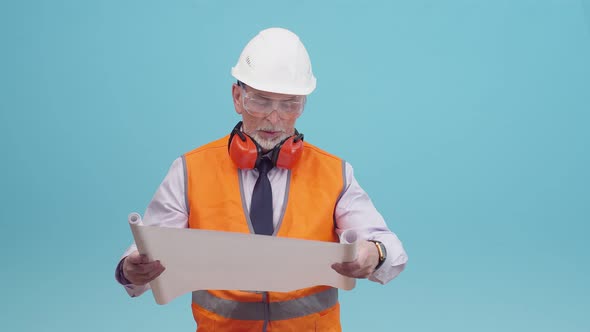 Adult engineer man in a working protective uniform, looks at schemes blueprint of the project