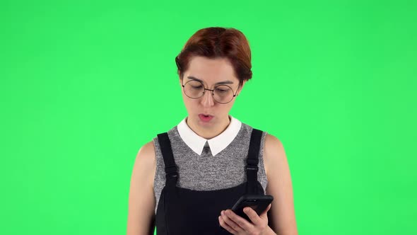 Portrait of Funny Girl in Round Glasses Is Angrily Texting on Her Phone. Green Screen