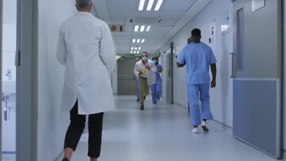 Diverse group of male and female doctors in face masks running through hospital corridor