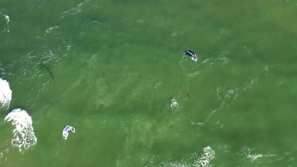 AERIAL: Top View Rotating Shot of Young People Kite Surfing Ride on Big Waves in the Baltic Sea