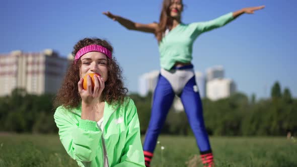 Joyful Confident Retro Sportswoman Juggling Smelling Tangerine Looking at Camera Smiling with Friend
