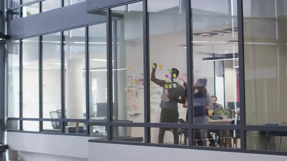 Diverse male and female work colleagues brainstorming using glass wall in meeting room