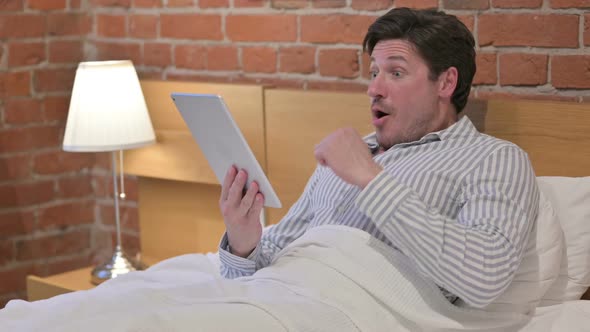 Middle Aged Man Celebrating Success on Tablet in Bed