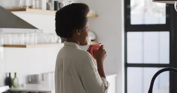 Happy african american woman drinking coffee in kitchen