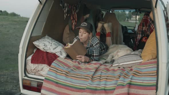 Woman Lying in Van with Dog and Reading Book