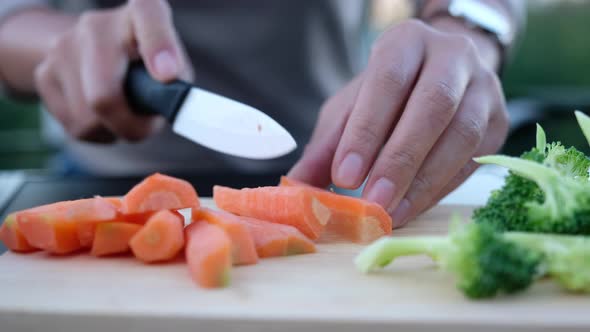 Closeup of a woman cutting and chopping carrot by knife on wooden board