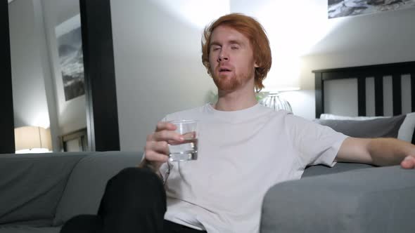 Pensive Man Drinking Water while Sitting on Couch