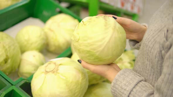 Young Woman in the Vegetable Department of a Supermarket Chooses a Cabbage