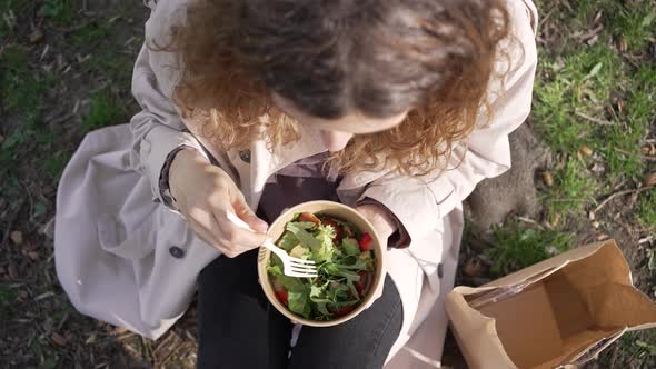 Woman Sits on Grass in City Park Eating Fresh Vegan Salad