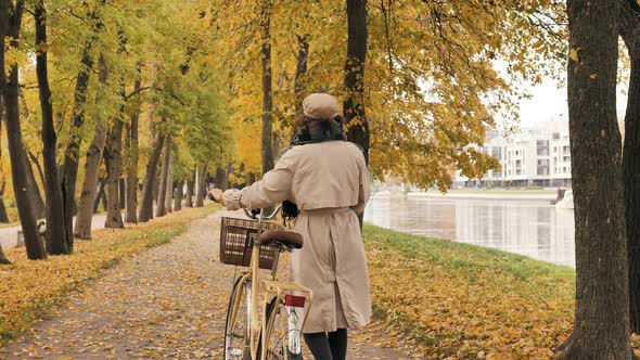 Young Woman Walks with Bike Against Yellow Trees in Park