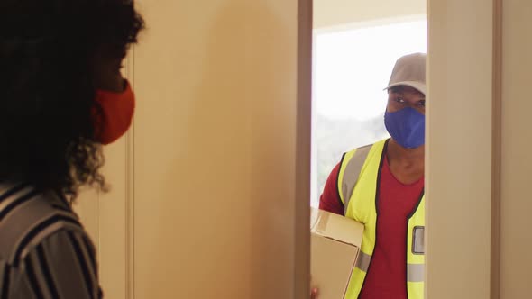 Delivery man wearing face mask delivering package to african american woman wearing face mask at hom