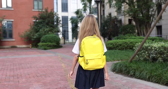 Happy Little Caucasian Blonde Girl Seven Years Old in Uniform with Yellow Backpack Going Back to