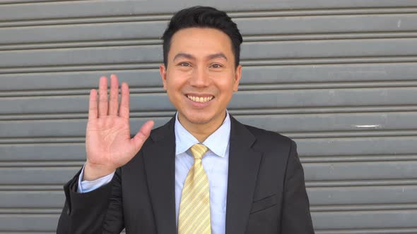 Asian smiling businessman waving hand to camera