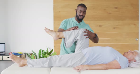 Video of african american male physiotherapist exercising with caucasian senior woman