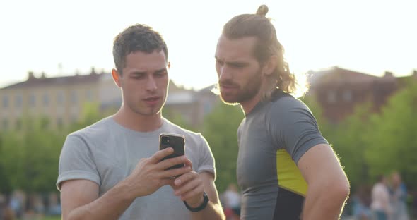 Young Male Friends Checking Sports App on Smartphone After Workout in Park