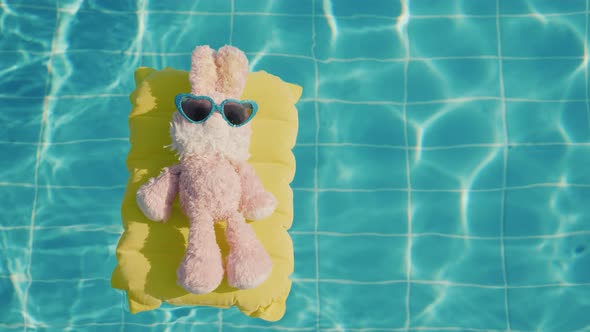 A Plush Bunny Floats on a Yellow Inflatable Mattress in the Pool