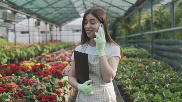 young girl with a folder for notes in her hands in a greenhouse talking on the phone on a background