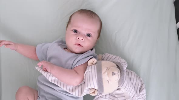 Newborn Baby Boy 3 Months Old Lies in Crib Nursery with Blue Clothes on His Back with Teddy Bear