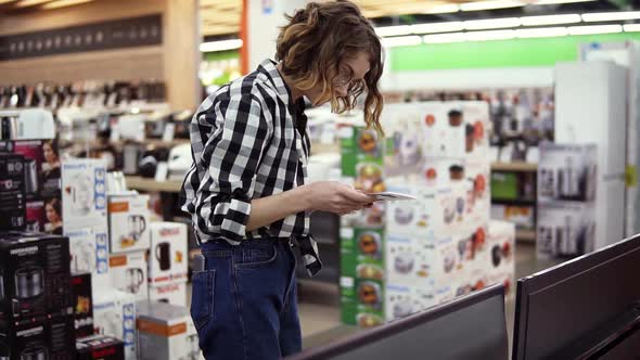 Curious Female Customer Choosing Large TVsets at Electronics Store Reading Instruction for It