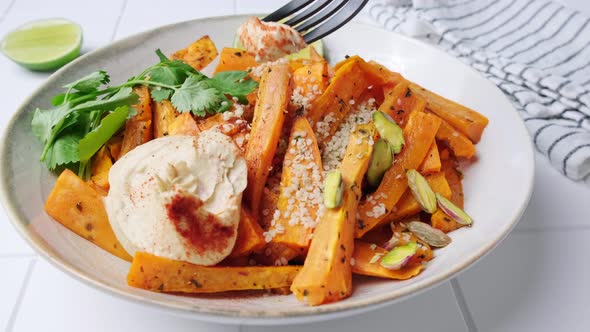 Baked sweet potato wedges with hummus, nuts and seeds in bowl.