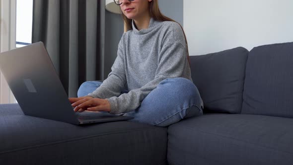 Woman Sitting on a Cozy Sofa and Working on a Laptop