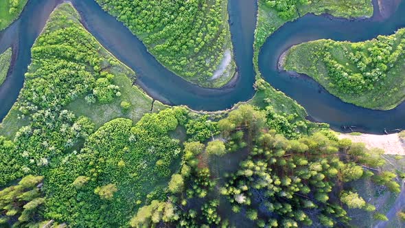 Rising aerial view of river winding through green meadow