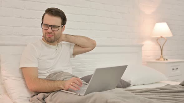 Young Man with Laptop Having Neck Pain in Bed