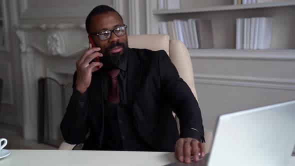 Adult Afro-american Man Is Communicating By Mobile Phone with Colleague and Checking Email in Laptop