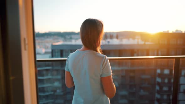 Woman with a Cup of Coffee or Tea Goes To the Balcony To Admire the Sunset