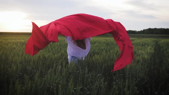 Young Girl Running with Red Tissue in Green Field. Happy Cute Girl Playing in the Wheat Field on a