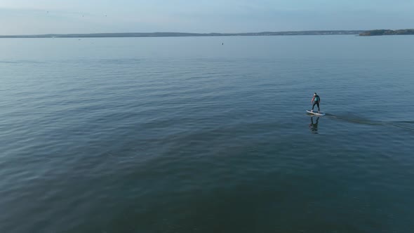 Man Standing Up on a Hydrofoil Surfboard on Large Blue Lake in Sunny Weather