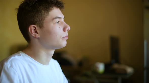 A teenager looks out the window and drinks tea at breakfast