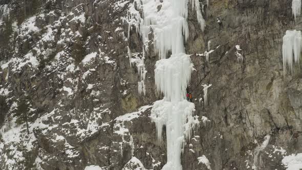 Two climbers standing on ledge of frozen cascade Aerial reveal sheer cliff