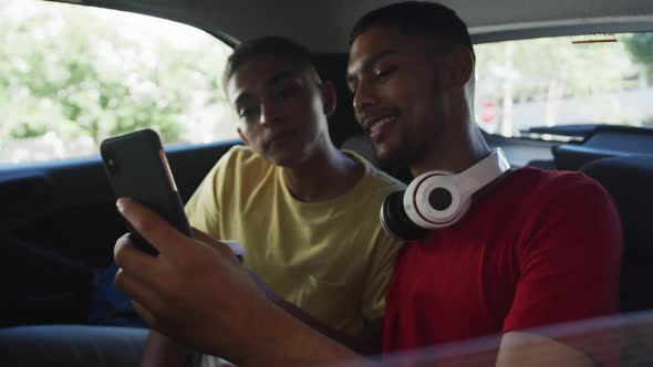 Two happy mixed race friends holding coffee and using smartphone in cab