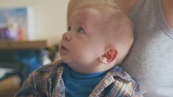 Cute Baby in Warm Clothes Sits on Mommy Knees in Room