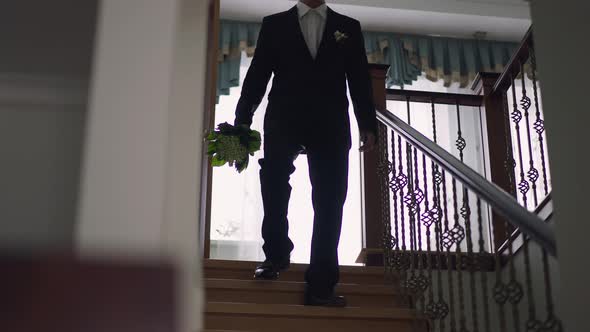 Young Confident Asian Groom in Elegant Costume with Boutonniere Walking Downstairs Holding Bouquet