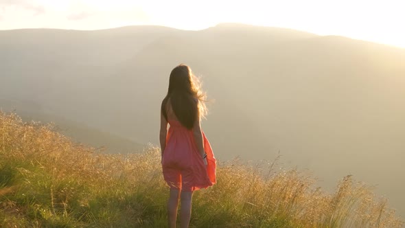 Young Woman in Red Dress Standing on Grassy Field on a Windy Evening in Autumn Mountains Enjoying