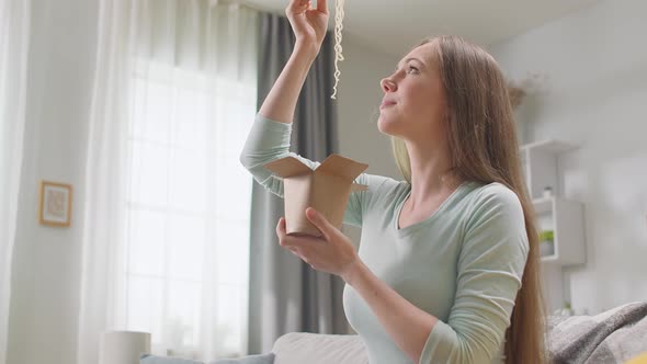 Woman Eating Noodles From a Box with Chopsticks at Living Room