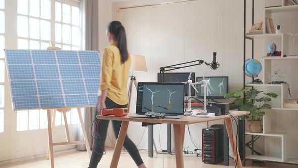 Asian Woman Walks Into The Office That Has Solar Cell Next To The Laptop Showing Wind Turbine