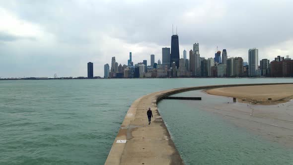 person walking around Lake Michigan, travel chicago downtown seen in the background, cloudy afternoo