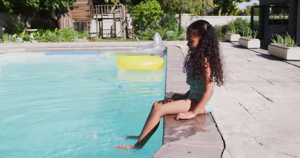 Happy biracial girl sitting by pool on a sunny day