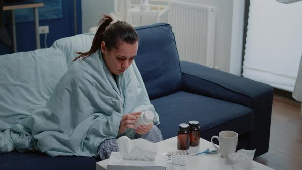 Sick Woman Reading Label on Bottle of Pills and Medicaments