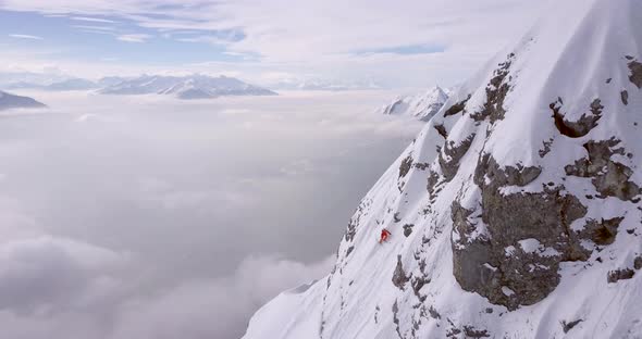 Aerial drone view of a skier skiing down a steep snow covered mountain.