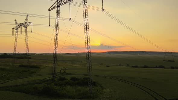 Dark silhouette of high voltage towers with electric power lines at sunrise.