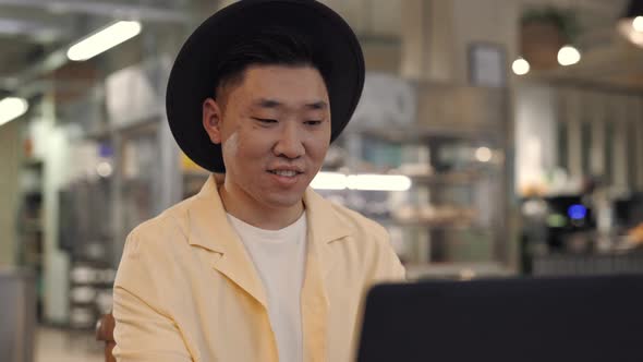 Happy Young Guy Sitting at Cafe and Working on Laptop