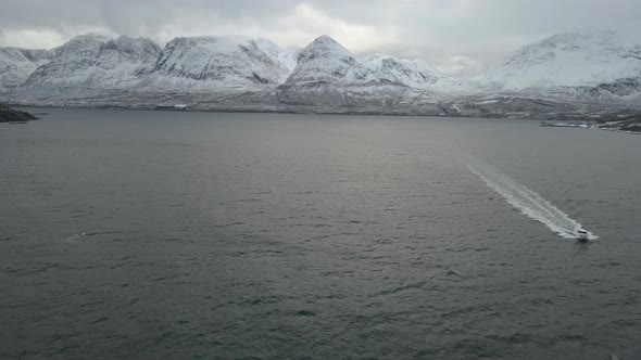 Cinematic drone shot crossing in front of racing speedboat in ocean, snowy mountain background