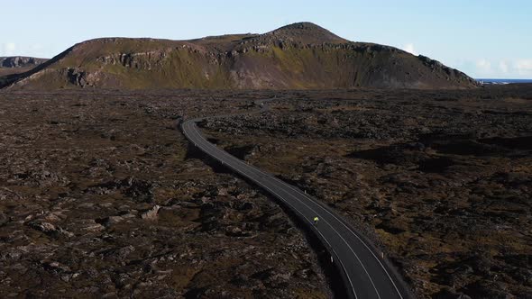 Cyclist riding on open road through volcanic landscape in Iceland, mountain in background, aerial