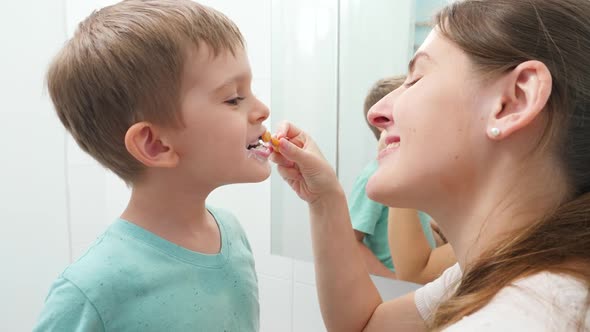 Young Caring Mother Brushing and Cleaning Teeth of Her Little Son