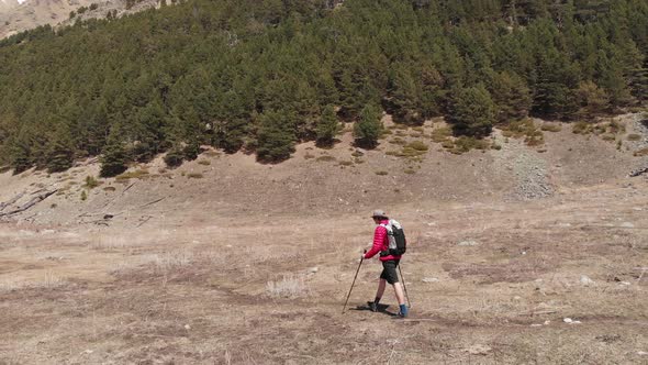 Aerial View of a Stylish Young Man in a Sunglasses Cap and Shorts with a Jacket Walks Trekking with